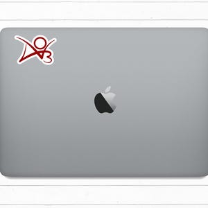 May include: A silver laptop computer with a red sticker on the top left corner. The sticker features a stylized red figure with a heart. The laptop has a black Apple logo in the center.