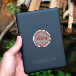 May include: A black e-reader with a red and white sticker that says "If there is a screen A03 can be seen".