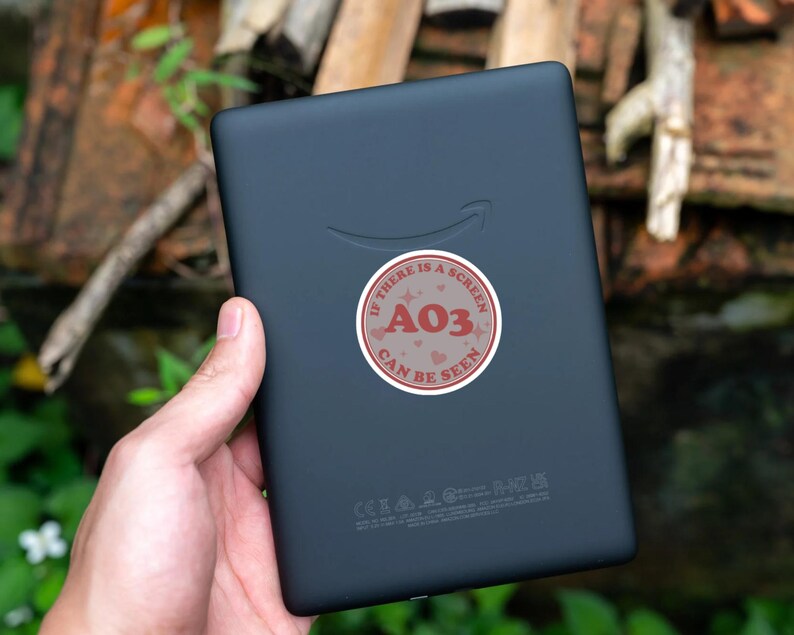 May include: A black e-reader with a red and white sticker that says "If there is a screen A03 can be seen".