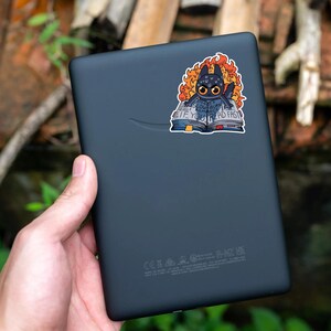 May include: A black Kindle e-reader with a sticker of a black dragon reading a book with the text "Read fast if you want to live".