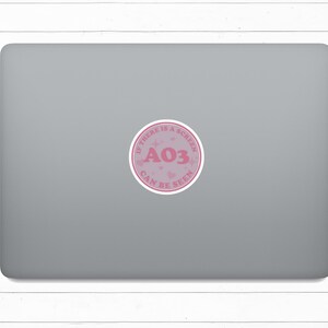 May include: A pink and white sticker with the text "If there is a screen, AO3 can be seen" on a silver laptop.