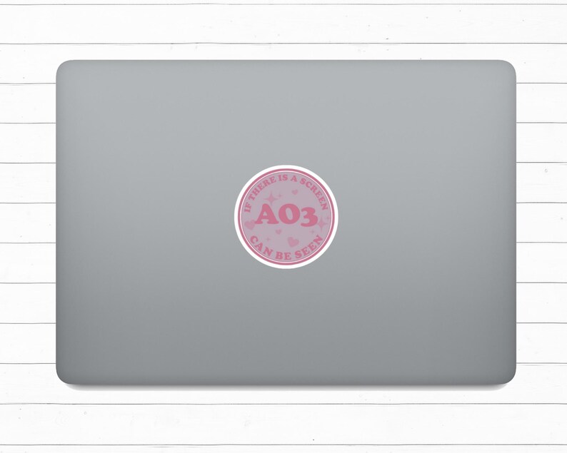 May include: A pink and white sticker with the text "If there is a screen, AO3 can be seen" on a silver laptop.