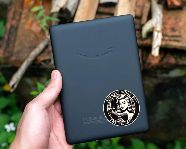 Op de afbeelding: Zwart-witte sticker met een vrouw die een boek leest. De sticker zegt "Always Falling For The Villain".