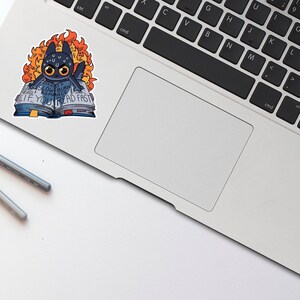 May include: A black and blue sticker of a cartoon dragon reading a book with the text "Glowburn Romance. If you read fast." The dragon is surrounded by flames.