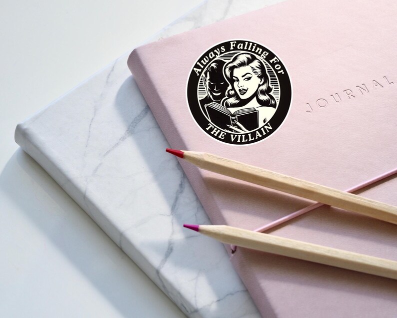Op de afbeelding: Een zwart-witte sticker met de tekst "Always Falling For The Villain" en een illustratie van een vrouw die een boek leest met een man achter haar.