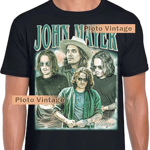 Puede incluir: Camiseta negra con un gráfico de estilo vintage de John Mayer. El diseño incluye múltiples imágenes del músico, con el nombre "John Mayer" en una fuente estilizada. La camiseta tiene un cuello redondo clásico.