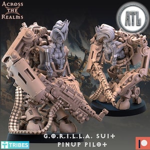 May include: Two beige-colored miniature figures of a woman in a mech suit, holding a large gun. The figures are labeled "G.O.R.I.L.L.A. SUIT + PINUP PILOT +" and "ACROSS THE REALMS" is printed at the top. The figures are on a black base.