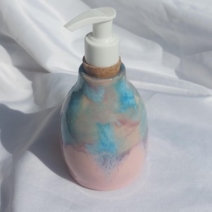 Peut inclure: Un distributeur de savon en céramique au corps arrondi, doté d'un émail rose pâle à la base qui se fond dans des nuances de bleu, de violet et de crème. Le sommet comprend un bouchon en liège équipé d'une pompe en plastique blanc.