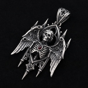 May include: A silver-toned pendant featuring a winged skeleton figure encased within an arched frame. The design includes a central oval red gemstone on the ribcage, multiple small black circular stones embedded in the wings, and a decorative bail.
