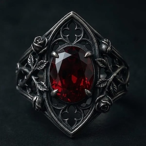 May include: A silver-toned ring featuring an oval, deep red gemstone set within an ornate, gothic-style frame. The ring is embellished with rose and leaf details, creating a vintage aesthetic. The design is intricate and detailed.
