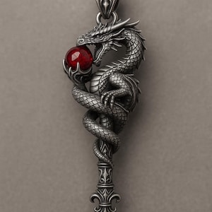 Könnte beinhalten: Silberfarbener Anhänger mit einem detaillierten Drachen, der sich um einen zentralen Stiel windet. Der Drache hält eine rote Kugel in seinen Krallen und im Maul. Der Anhänger hat ein verziertes Design und hängt an einer Kette.