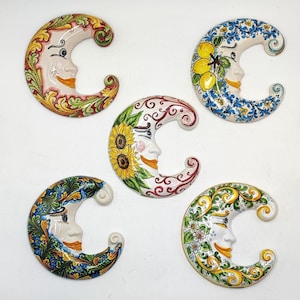Può includere: Cinque decorazioni murali a forma di luna crescente in ceramica. Ogni luna presenta un volto sorridente ed è decorata con colorati disegni floreali e fruttati. La tavolozza dei colori comprende giallo, blu, verde e rosso.