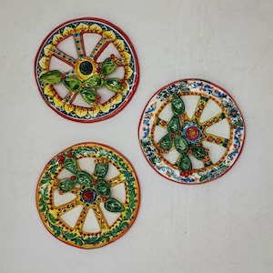 Könnte beinhalten: Drei dekorative Keramikplatten mit einem Raddesign. Jede Platte hat einen weißen Hintergrund mit einem farbenfrohen Rand und Speichen. Die Platten haben ein grünes Kaktusdesign in der Mitte mit roten und gelben Akzenten.