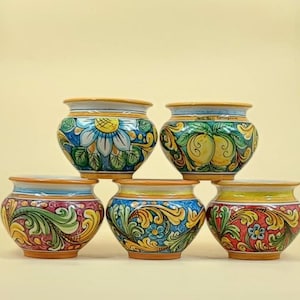 Può includere: Cinque vasi in ceramica con colorati disegni floreali e di frutta. Ogni vaso presenta un motivo unico di fiori, foglie e frutta nei toni del blu, verde, giallo e rosso. I vasi hanno una forma arrotondata e un bordo chiaro.