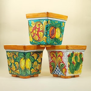 May include: Three square ceramic planters with hand-painted designs. The planters feature vibrant colors, including teal, yellow, orange, and green. Each planter has a different fruit or plant design, such as lemons, peaches, and cacti. The rims are painted orange.