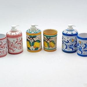May include: Set of four ceramic bathroom accessories in pink, yellow, and blue with floral and lemon designs. The set includes two soap dispensers and two toothbrush holders.