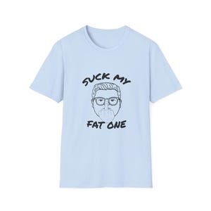 Puede incluir: Camiseta azul claro con un gráfico negro. El gráfico presenta una ilustración de dibujos animados de una persona con gafas, mostrando el dedo medio, y el texto "SUCK MY FAT ONE".
