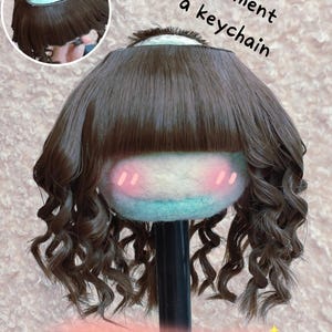 May include: A doll head with brown curly hair, a blue and white face, and pink blush marks. The text reads "Compartment for a keychain" and "Around the head 8.5" - 9".
