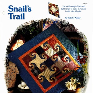 Pode incluir: Um cobertor colorido com fundo azul e um padrão de espirais vermelhas, laranja, amarelas e brancas. O cobertor é intitulado "Snail's Trail" e é de Jodi G. Warner. O texto "Basics & Beyond" está na parte inferior da imagem.