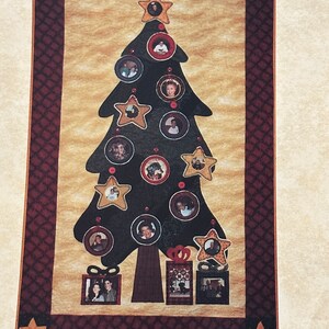 May include: A black silhouette of a Christmas tree with a brown trunk and red and gold ornaments. The ornaments are decorated with photos of people. There are also two presents with photos of people under the tree.