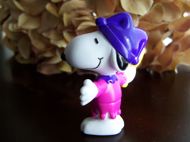 May include: A white and purple cartoon character with a purple hat and a pink dress. The character is holding a yellow object in its right hand.