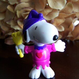 May include: A white and purple cartoon character wearing a pink dress with a heart on the front and holding a yellow wand.