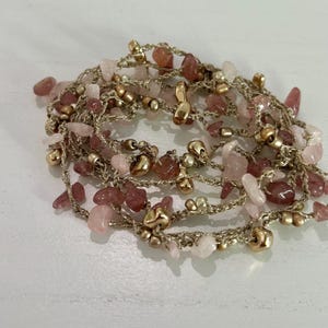 May include: A necklace featuring a delicate design with pink and rose quartz gemstones, interspersed with gold-colored beads. The necklace is crafted with a woven, metallic thread, creating a layered effect. The gemstones vary in size and shape, adding visual interest.