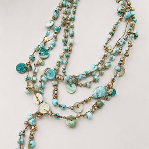 May include: A multi-strand necklace featuring turquoise-colored stone beads, flat circular shell-like discs, and small metallic beads strung on a thin, dark cord. The design includes several draped layers and dangling ends with assorted beads.