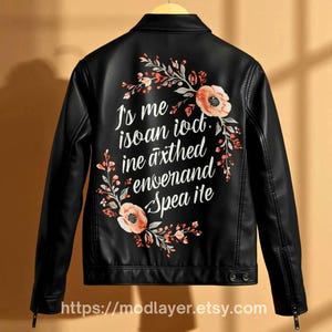 women black leather jacket with floral and typography fusion print, inspirational quote text surrounded by light hand-paint floral artwork, jacket hanging on wooden hanger.