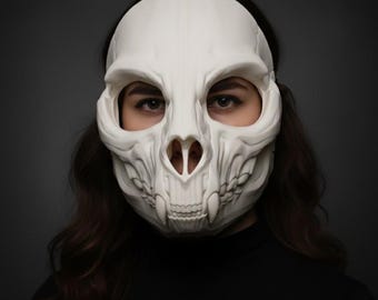 Könnte beinhalten: Eine weiße, dreidimensionale Tierschädelmaske mit markanten Augenhöhlen, einer detaillierten Nasenhöhle und spitzen Zähnen. Die Maske bedeckt den oberen Teil des Gesichts, wobei die Augen darunter sichtbar bleiben, und besteht aus glatten Oberflächen.