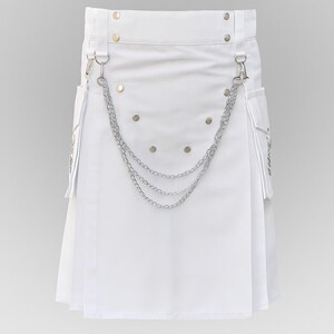 May include: A white kilt with silver chain detailing and pockets. The kilt features silver rivets and metal hardware. The design includes a pleated front and a chain that hangs across the front. The kilt is made of a smooth, solid white material.