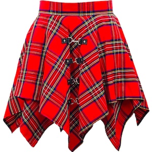 Puede incluir: Falda a cuadros roja con un dobladillo asimétrico. La falda presenta correas de cuero negro con anillos y hebillas de metal plateado. El patrón de cuadros incluye líneas rojas, amarillas, azules y blancas.