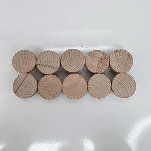 May include: A set of ten circular wooden discs arranged in two rows of five. Each disc features a light tan color with visible natural wood grain patterns, smooth flat surfaces, and rounded edges, showcasing the organic texture of the raw wood material.