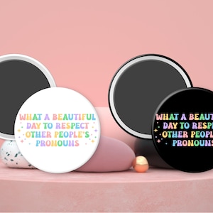 May include: Two round magnets with a white background and a black background. Both magnets feature the text "WHAT A BEAUTIFUL DAY TO RESPECT OTHER PEOPLE'S PRONOUNS" in rainbow colors.
