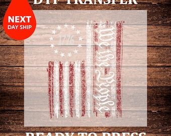 May include: DTF transfer design featuring a distressed American flag with the text "We the People" and "1776". The design is in red, white, and blue, with the words "Ready to Press" at the bottom. The image also includes a red teardrop with the words "Next Day Ship".