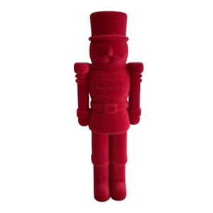 May include: A red velvet nutcracker figurine. The figurine is in the shape of a soldier, with a tall hat, mustache, and a belt. The nutcracker is a festive decoration.
