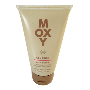 Puede incluir: Un tubo beige de exfoliante facial MOXY. El tubo tiene una tapa marrón y el texto "MOXY" en letras marrones grandes. Debajo está "ALL SKIN" y "FACE SCRUB PINEAPPLE EXTRACT + CRUSHED APRICOT PITS". El tubo contiene 118 ml.