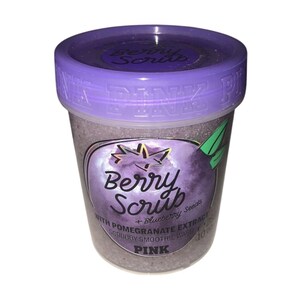 Op de afbeelding: Een doorzichtige plastic pot met Pink Berry Scrub en een paarse deksel. Het etiket toont "Berry Scrub" en "WITH POMEGRANATE EXTRACT + Blueberry Seeds SCRUBBY SMOOTHIE WASH". De pot bevat ongeveer 283 gram product.