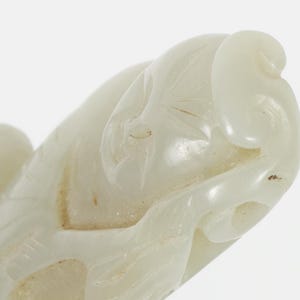 May include: Close-up of a carved, off-white sculpture. The sculpture has a smooth, polished surface with intricate floral or leaf-like details. The form is organic and flowing, with rounded shapes and subtle variations in texture.