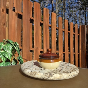 May include: A small brown and white ceramic crock pot with a lid. The crock pot is sitting on a granite surface.
