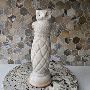 May include: A cream-colored owl figurine with a textured, crackled surface. The owl has large eyes and a detailed body, standing on a round base. The figurine is approximately 10 inches tall, perfect for home decor.