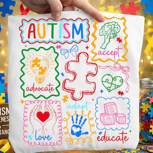 May include: White tote bag with colorful text and graphics related to autism awareness. The bag features the word "AUTISM" in rainbow colors, along with puzzle pieces, a lightbulb, a brain, and the words "advocate", "accept", "love", "adapt", and "educate".
