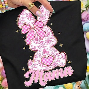 May include: Black t-shirt featuring a pink floral bunny design with a gingham bow and heart. The word "Mama" is written in pink script with a gold outline. Gold stars are scattered around the bunny.