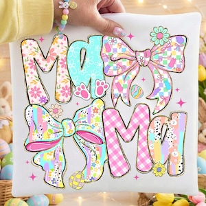 Puede incluir: Cojín blanco con la palabra "Mama" en un diseño colorido con patrones florales, lazos y elementos de Pascua. El diseño incluye huellas de patas y huevos. El cojín lo sostiene una persona que lleva una camisa amarilla y una pulsera pastel.