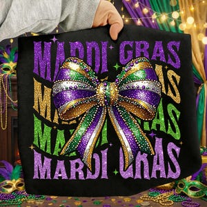 Puede incluir: Bolso tote negro con un gran lazo brillante en los colores de Mardi Gras: morado, verde y dorado. Las palabras "MARDI GRAS" están impresas en purpurina morada, verde y dorada. El bolso lo sostiene una persona.