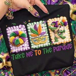 以下が含まれることがあります： 黒いTシャツ。マルディグラのデザインが施された3つの刺繍パッチが付いています。パッチには、カラフルな花輪、羽のマスク、風船を持った漫画のアリゲーターが含まれています。テキストは「Take me to the parade」と書かれています。