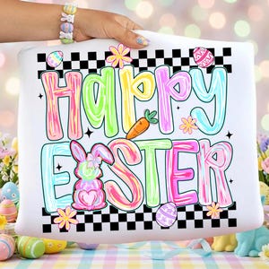 Może przedstawiać: Biała poduszka z napisem "Happy Easter" w kolorowych literach. Projekt zawiera kr&oacute;lika, marchewkę i pisanki, z czarno-białą szachownicą.