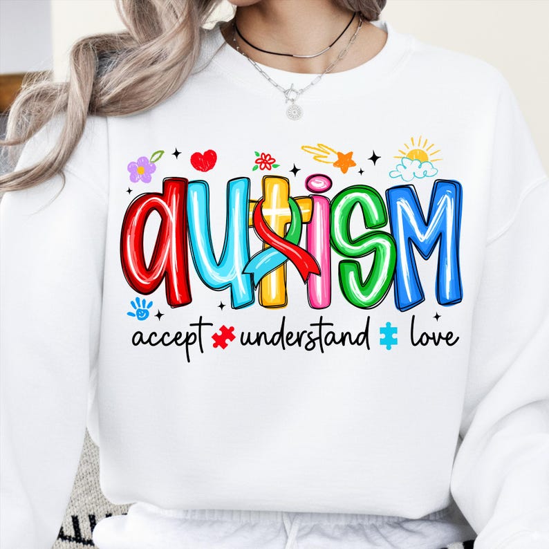 May include: White sweatshirt with the word "AUTISM" in colorful bubble letters. The design includes a red ribbon, flowers, hearts, stars, and the phrases "accept", "understand", and "love".