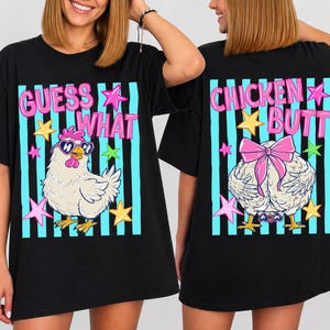 May include: Black t-shirt with a whimsical design. The front features the text "GUESS WHAT" above a cartoon chicken wearing sunglasses. The back displays "CHICKEN BUTT" above a chicken's rear with a pink bow. Accented with stars.