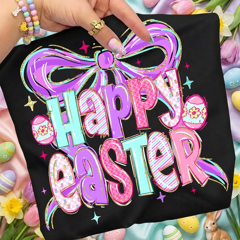 May include: Black t-shirt with a colourful "Happy Easter" graphic. The design features a large purple bow, pastel eggs, and the text in pink, blue, and purple with gold accents. The shirt is decorated with stars.